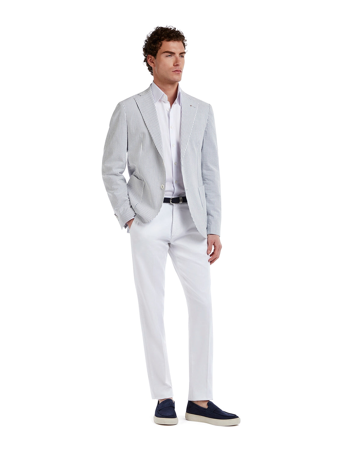 Men's striped blue and white blazer with a pale shirt and white trousers, styled with navy slip-on shoes.