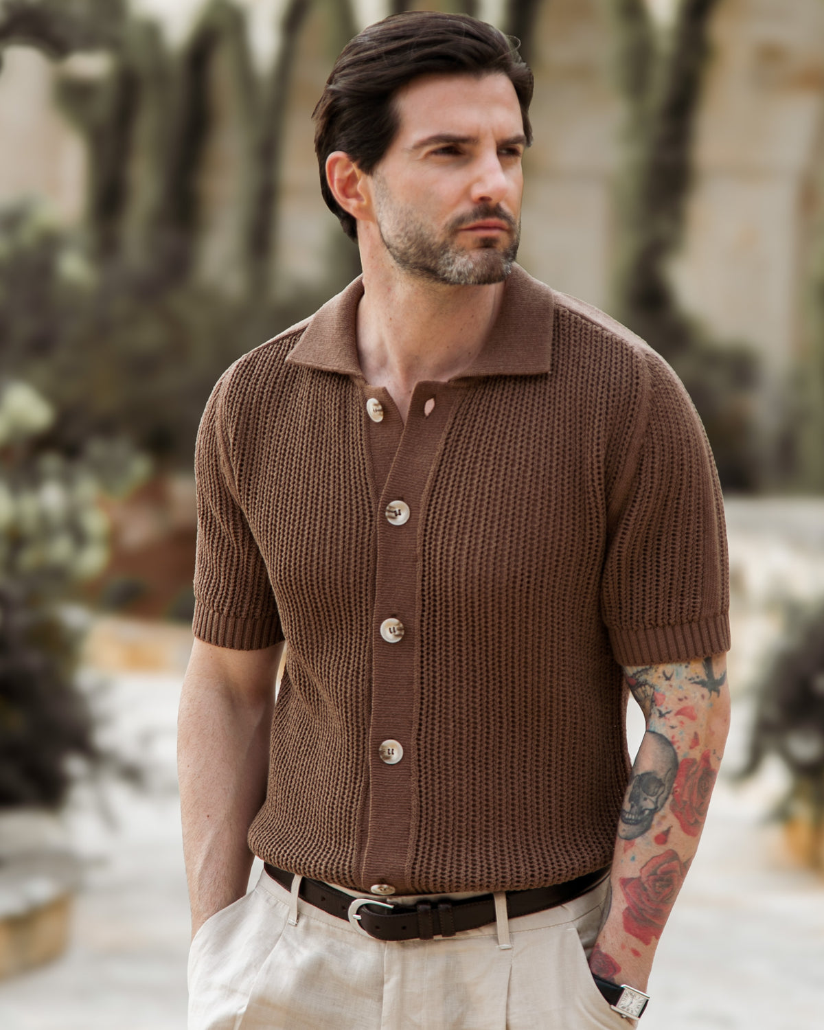 Men's brown waffle knit short sleeve polo shirt with button placket, paired with cream trousers and leather belt.