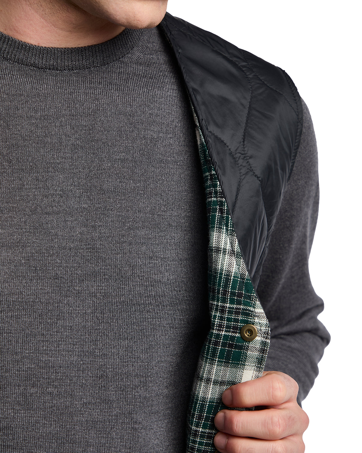 Men's quilted black vest over gray sweater with green and white plaid lining. Stylish, casual layering piece.