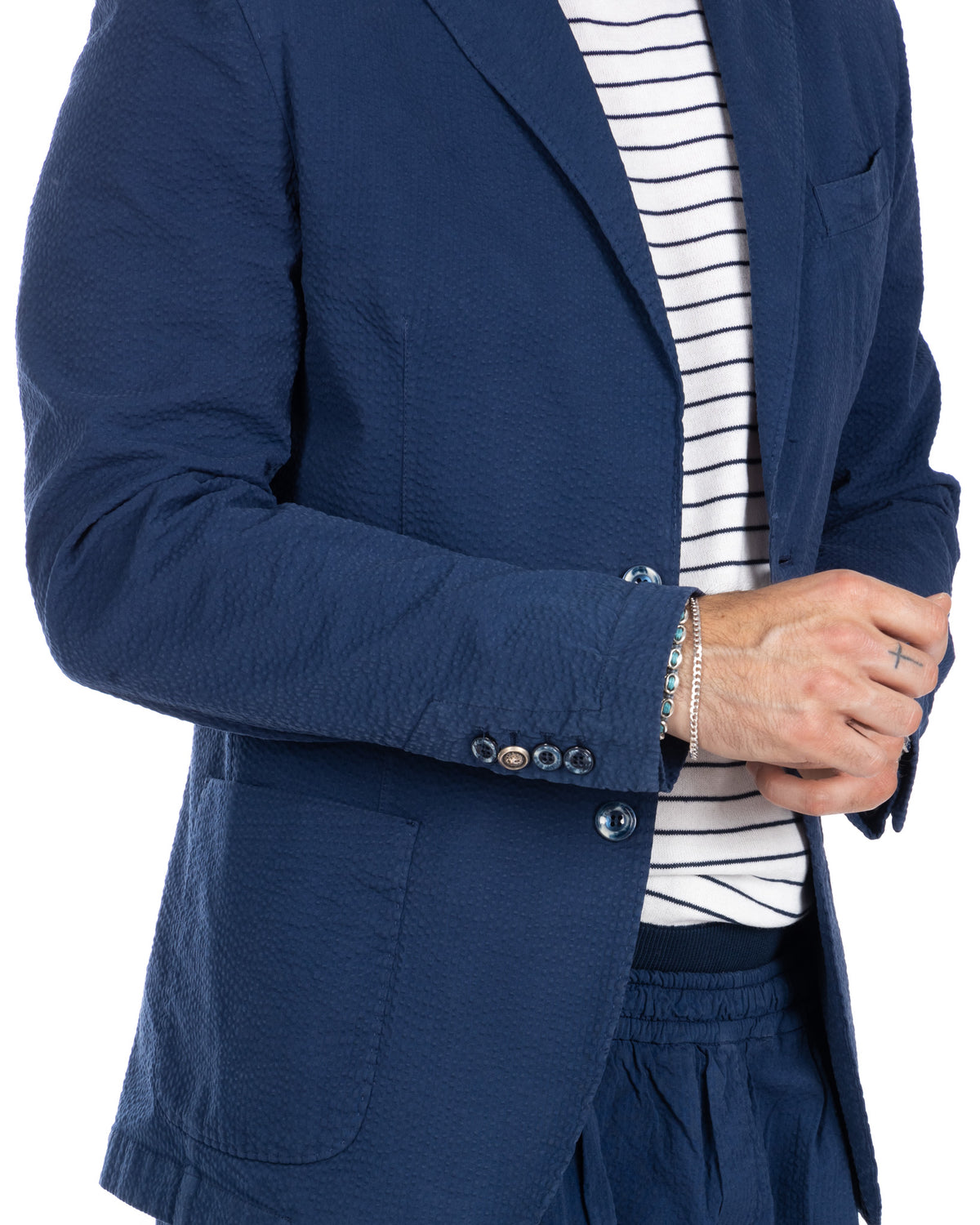 Navy blue textured seersucker blazer with notched lapels, paired with striped shirt. Unlined summer jacket with button.