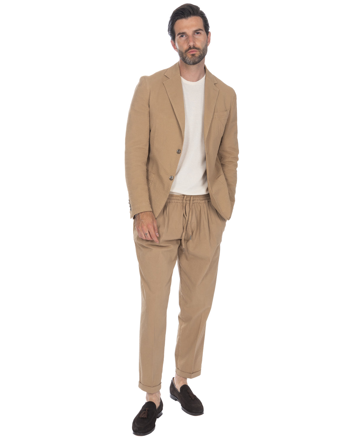 Men's beige seersucker suit with relaxed-fit drawstring pants, white knit tee, and black suede loafers.