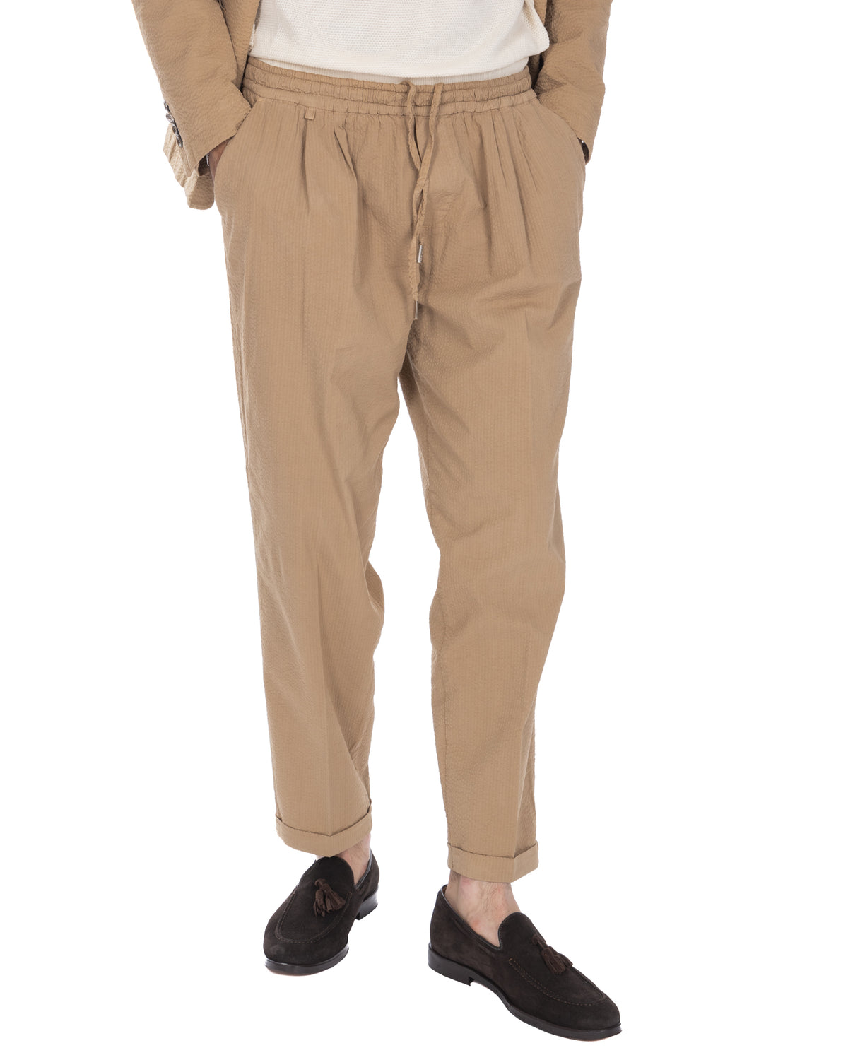 Beige seersucker drawstring pants with elastic waist, pleated front, and cuffed ankles. Relaxed fit casual trousers.