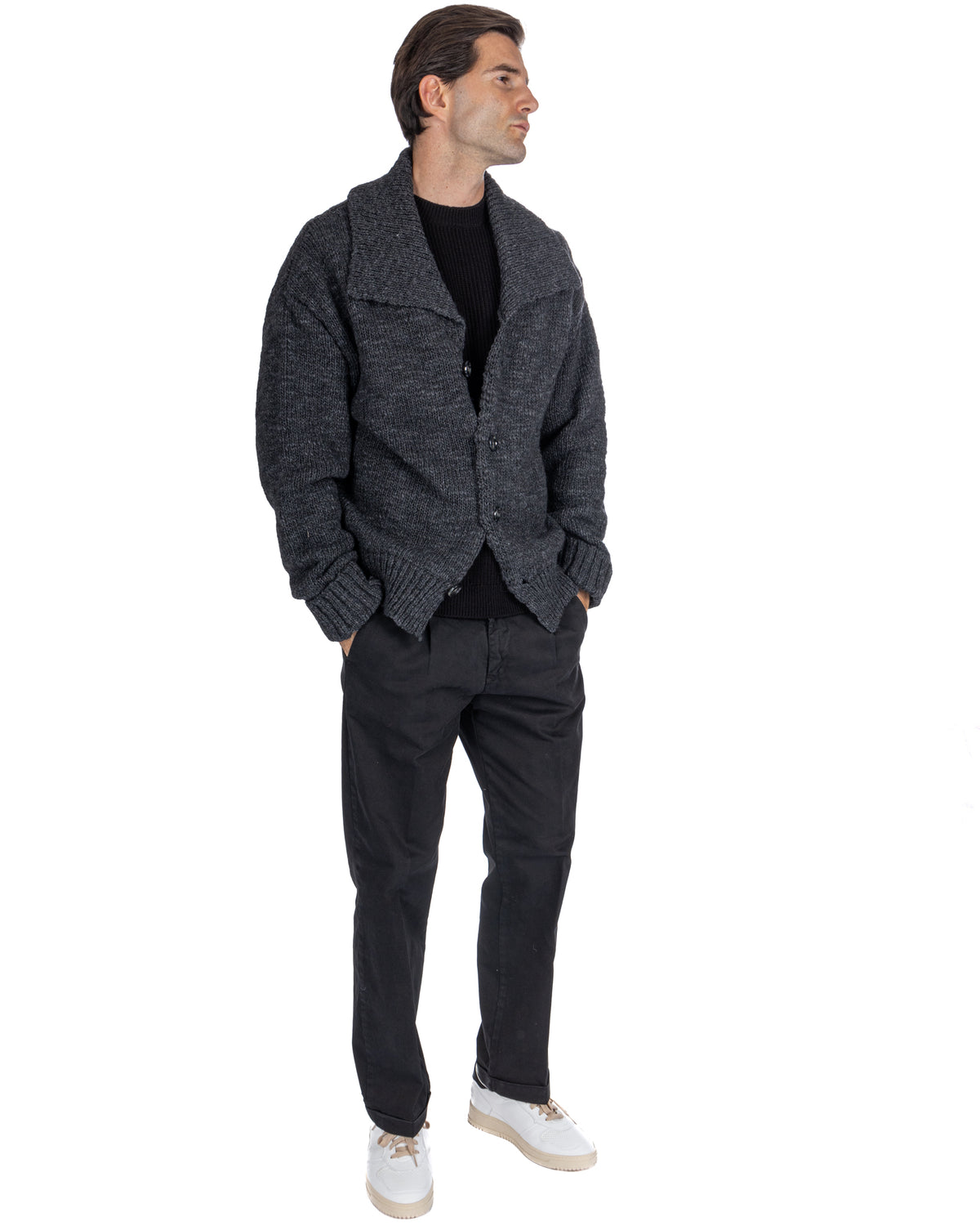Men's charcoal chunky knit wool cardigan with shawl collar, worn over black sweater and trousers.