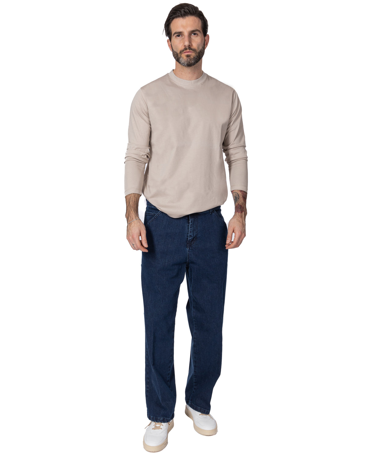 Men's beige long-sleeve cotton shirt with dark blue straight-leg jeans and white sneakers, casual outfit.