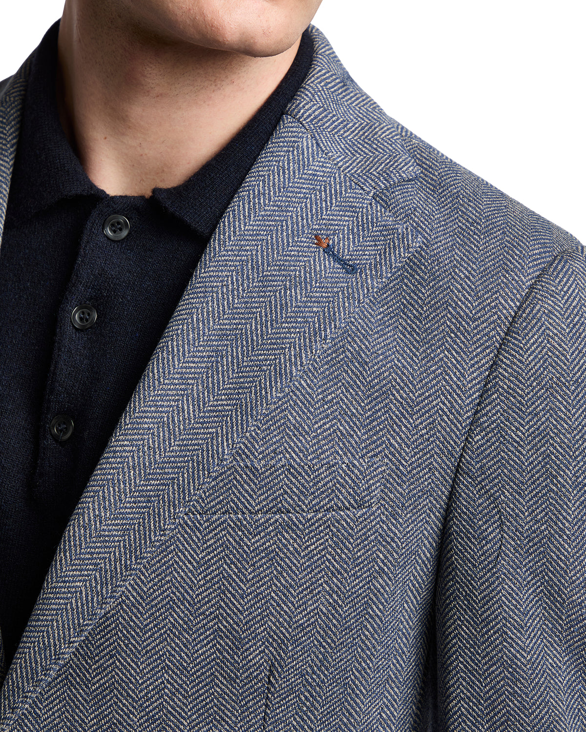 Blue herringbone blazer with a notch lapel, styled over a dark knit polo shirt. Elegant and modern men's fashion.
