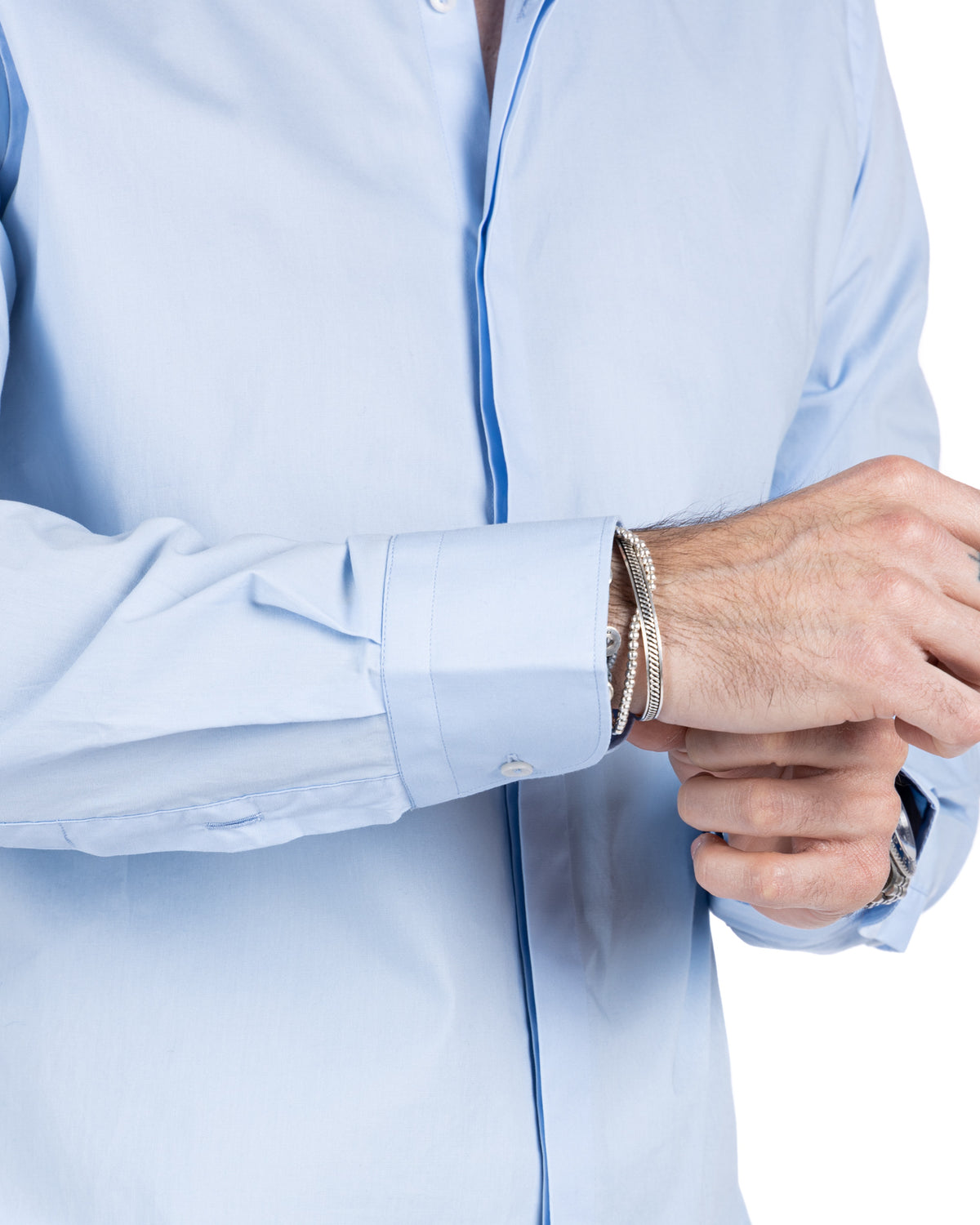 Close-up detail of a light blue cotton shirt with buttoned barrel cuff, worn with silver bracelets