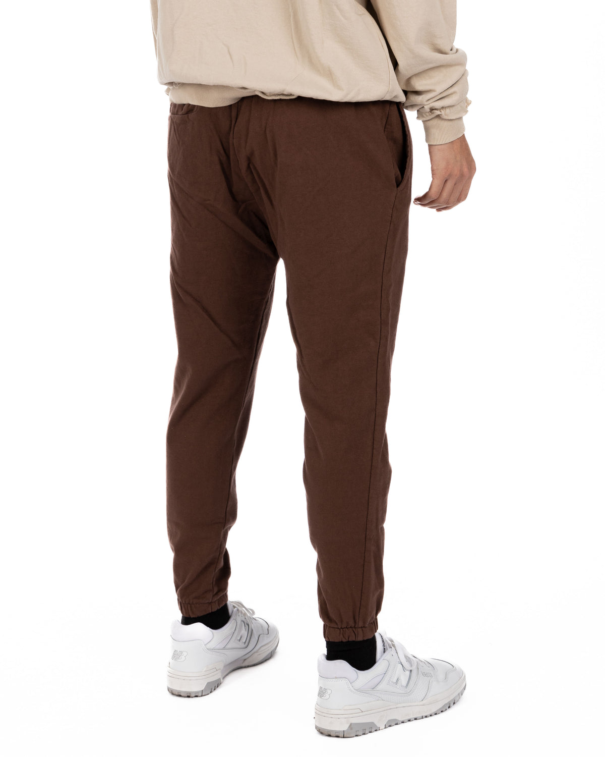 Brown cotton joggers with elastic waist and cuffed ankles, back view on model with white sneakers