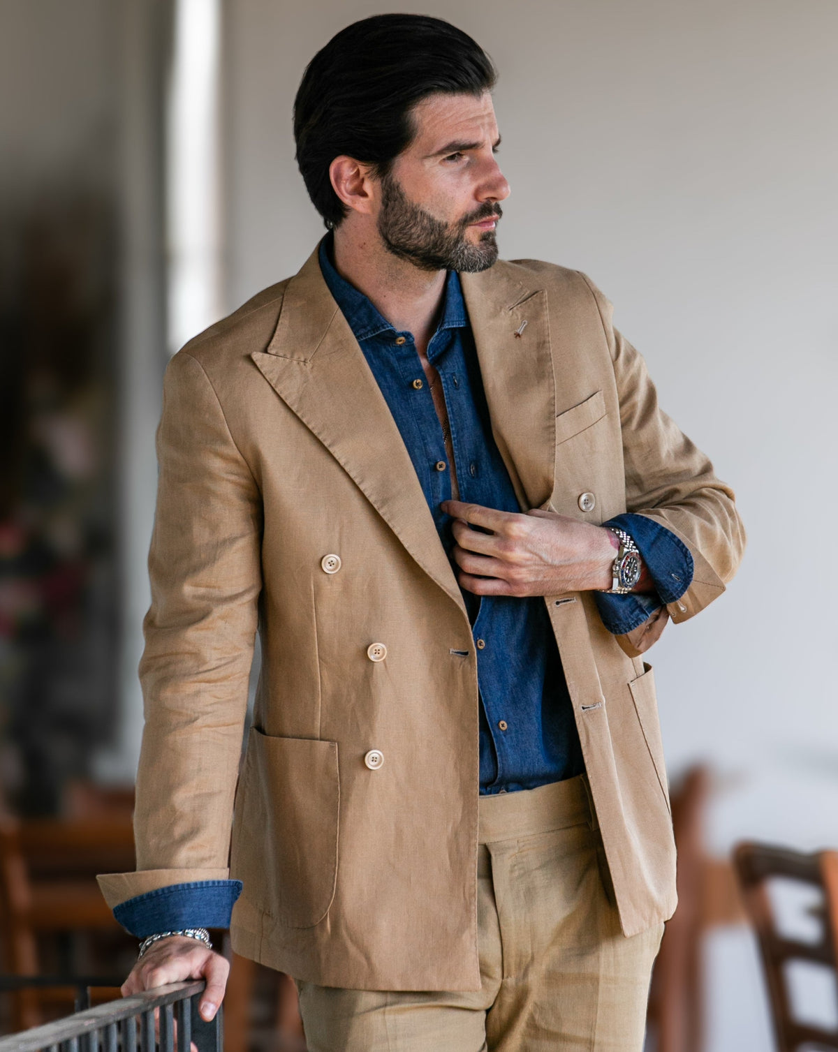 Tan linen double-breasted suit with blue denim shirt, peak lapels, and brass buttons for men's formal wear.