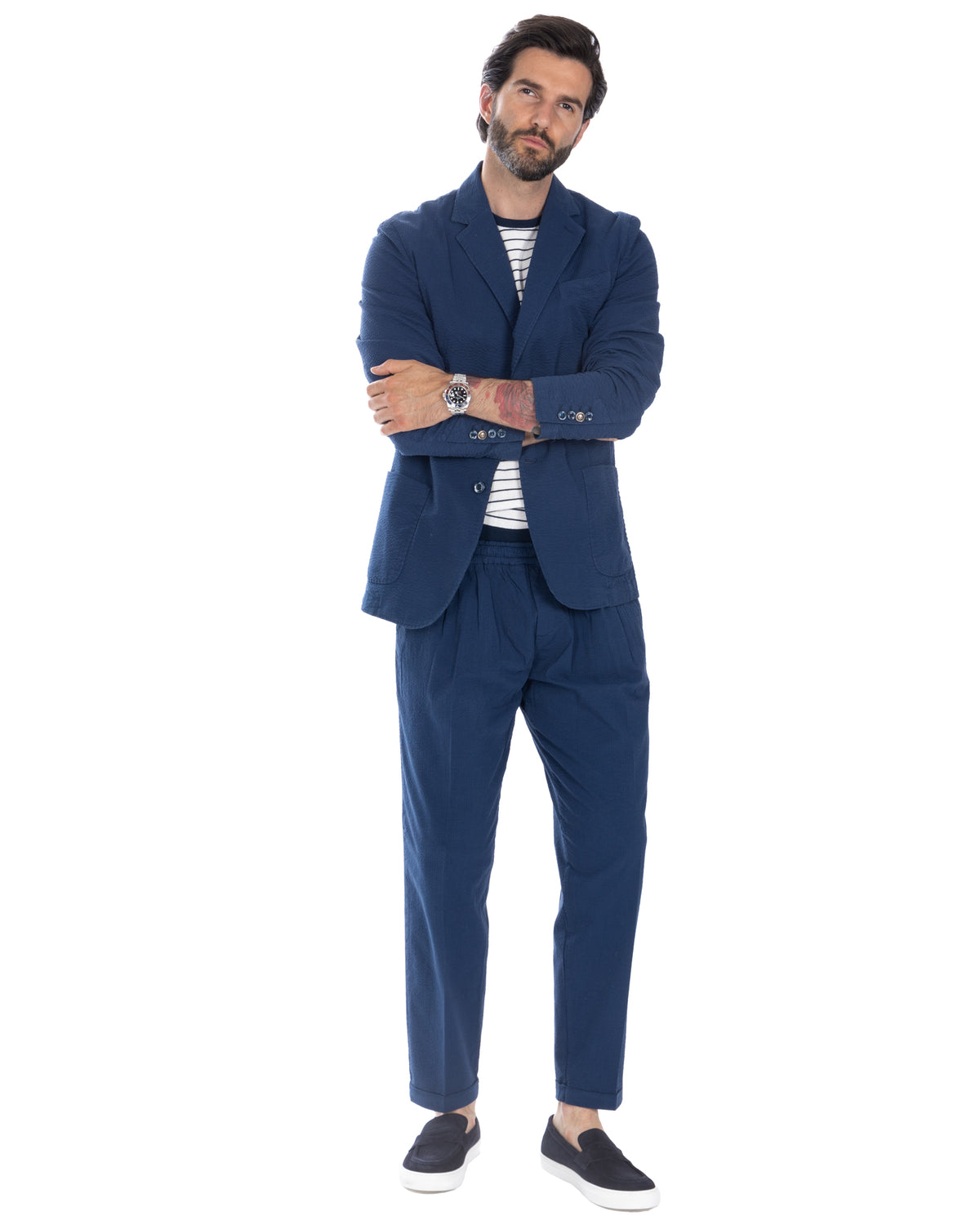 Navy blue textured linen suit with relaxed fit, paired with striped tee and black slip-on sneakers for smart casual style.