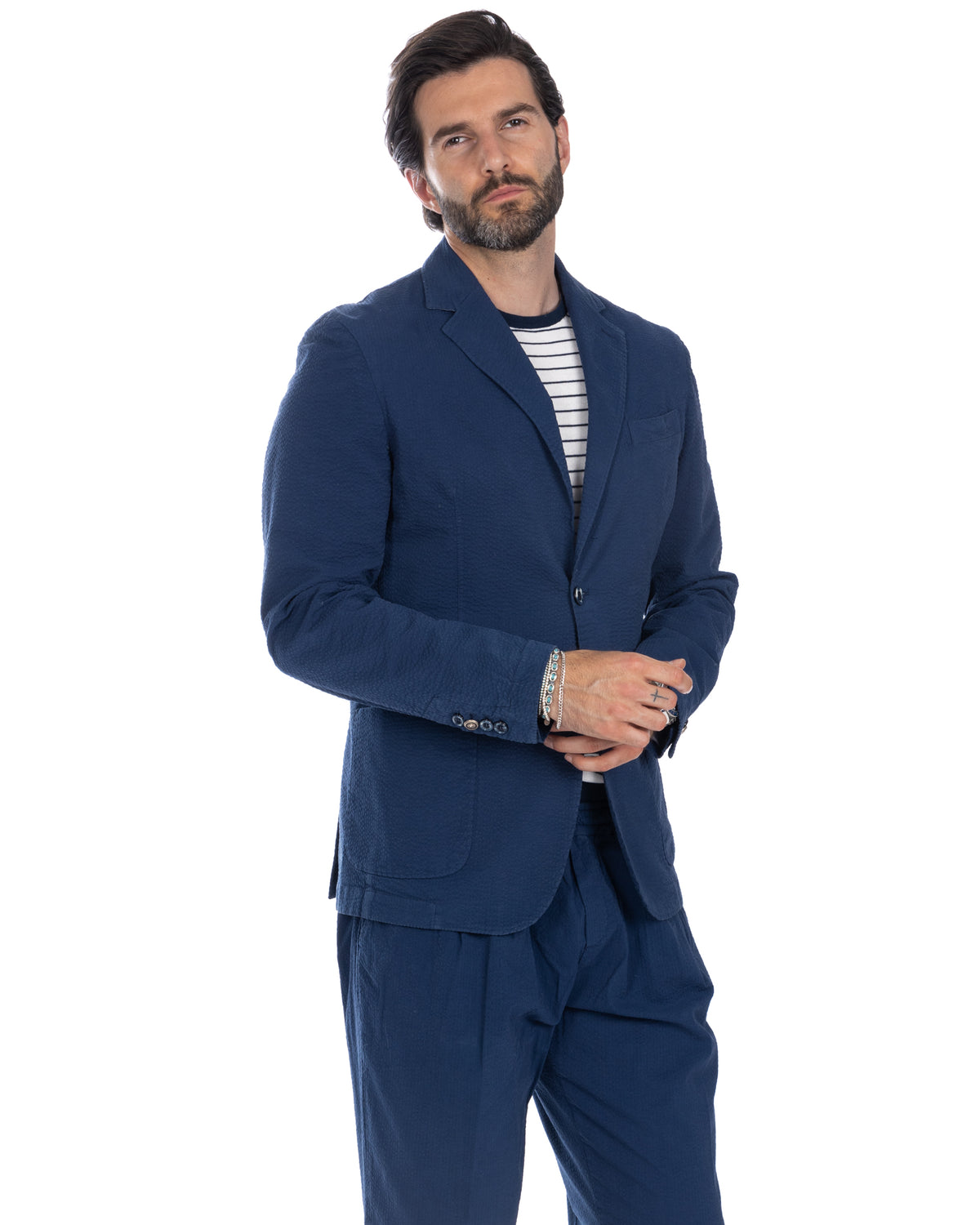 Navy blue textured linen suit with notched lapels, paired with striped tee. Relaxed fit blazer and matching trousers.