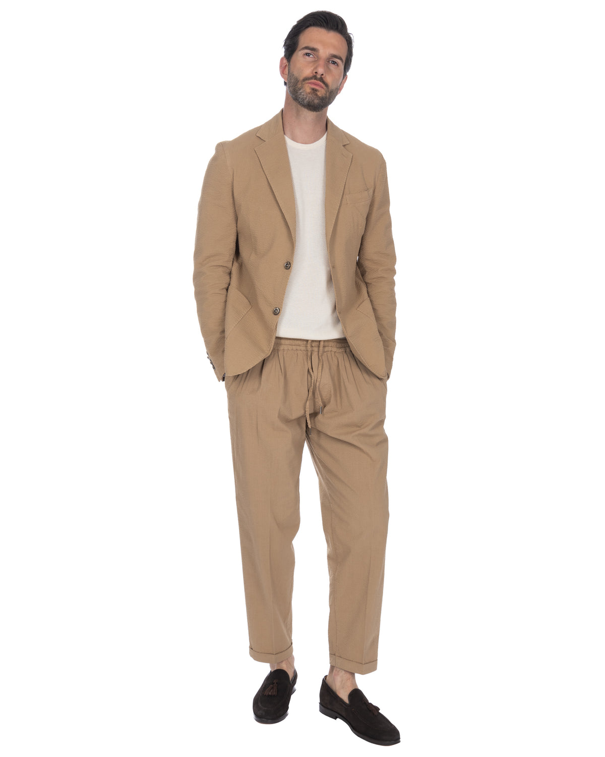 Men's beige seersucker suit with relaxed drawstring trousers, white knit tee, and black suede loafers.
