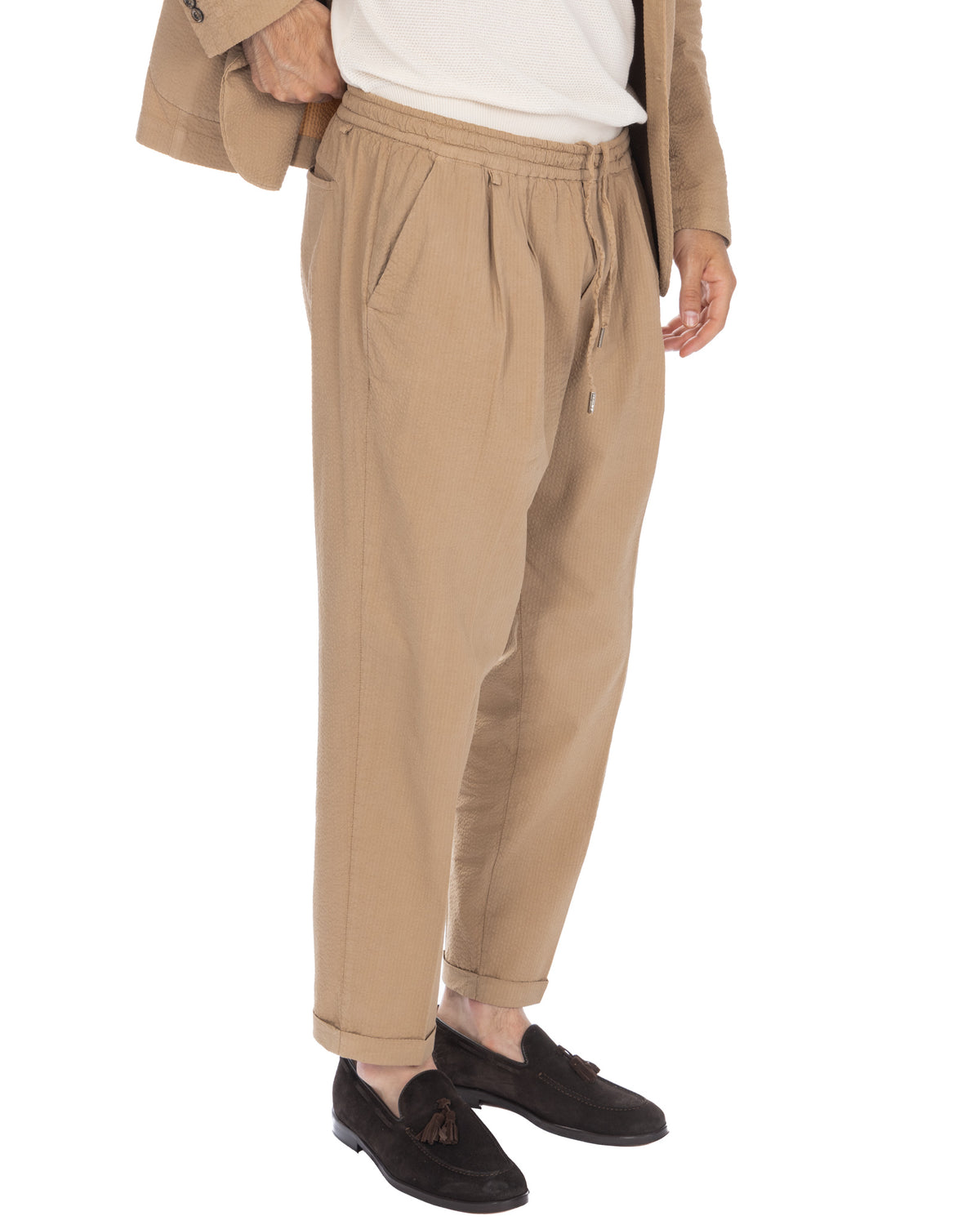 Beige cotton drawstring trousers with elastic waist, pleated front, and cuffed ankles. Relaxed fit casual pants.
