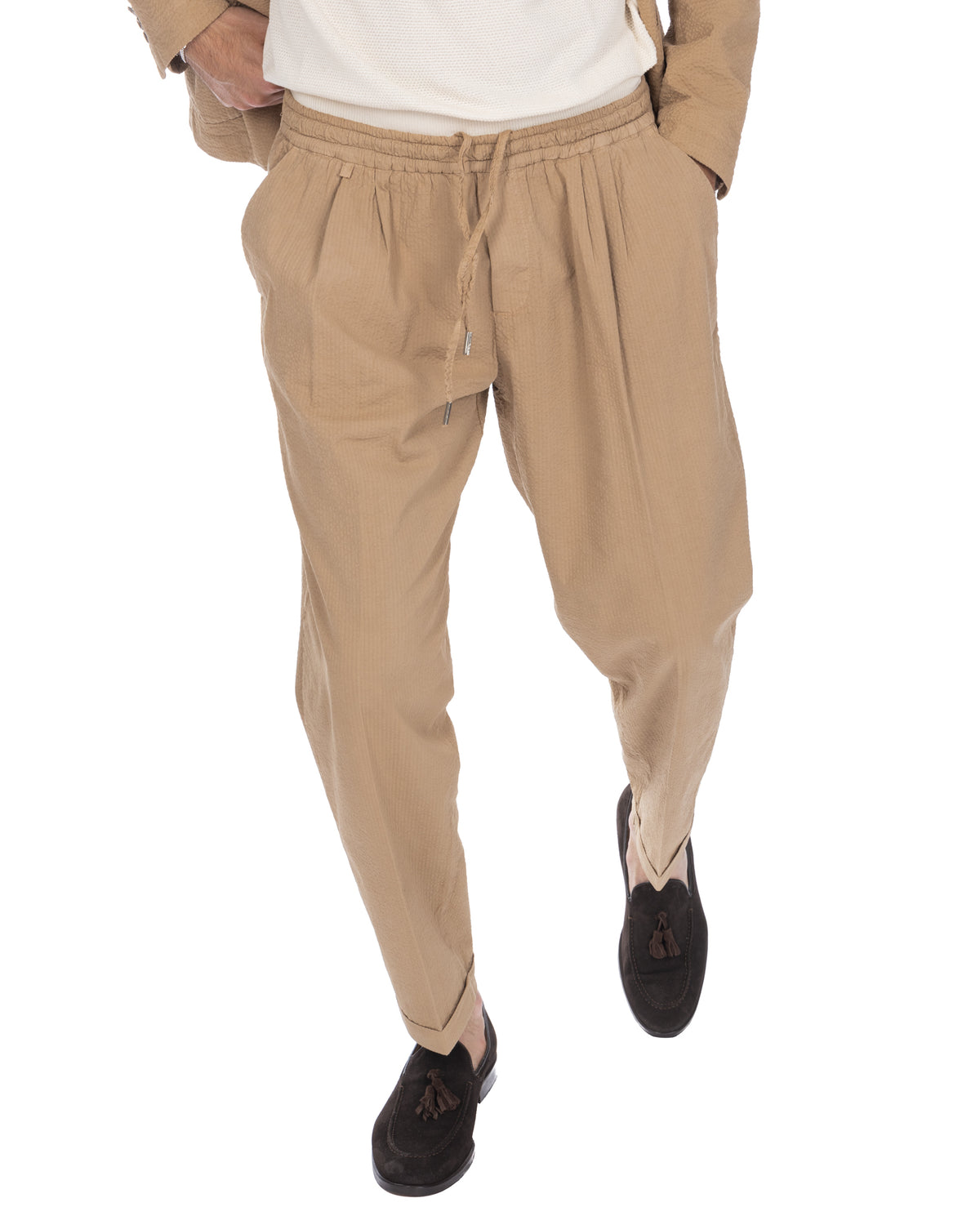 Beige seersucker drawstring pants with elastic waist, pleated front, and tapered leg. Lightweight summer trousers in tan.