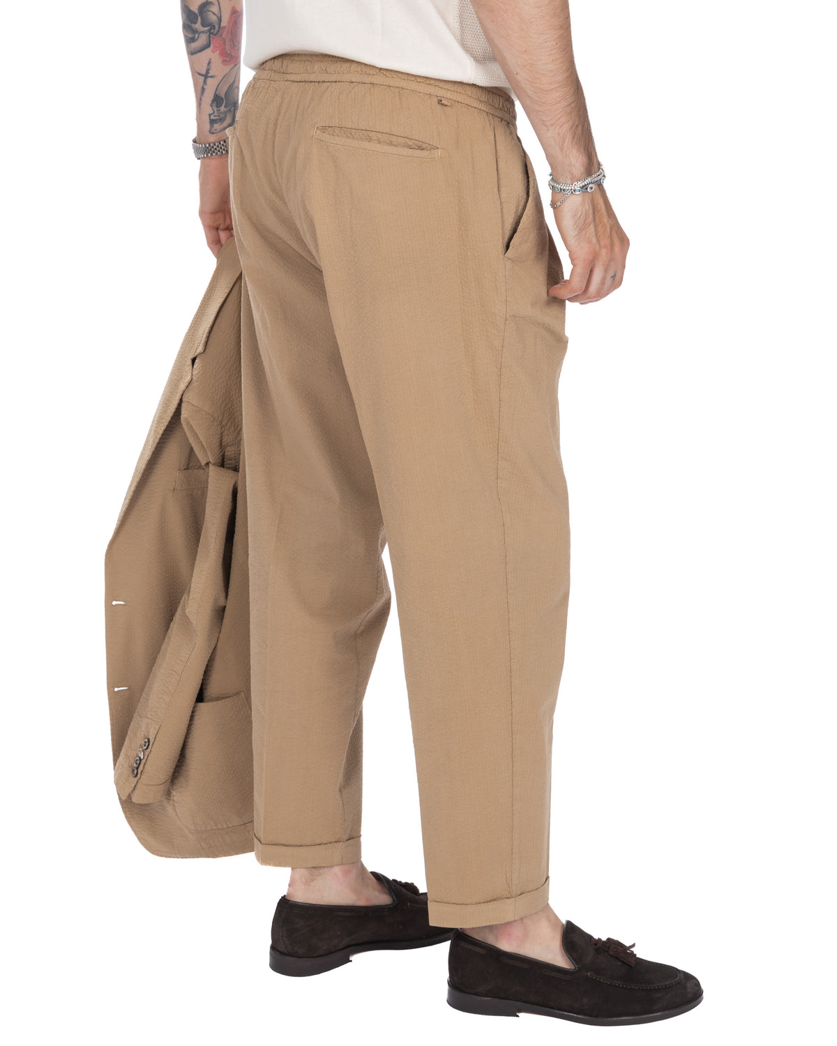 Men's beige relaxed-fit cotton trousers with elastic waist, side pockets, and cuffed hems. Casual tailored style.