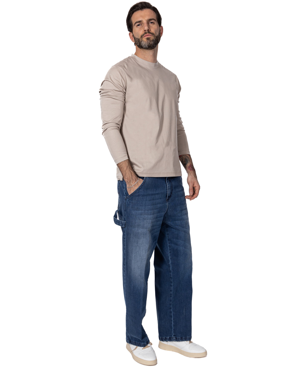 Man wearing beige cotton long-sleeve shirt with dark blue baggy denim jeans and white sneakers, casual streetwear style.