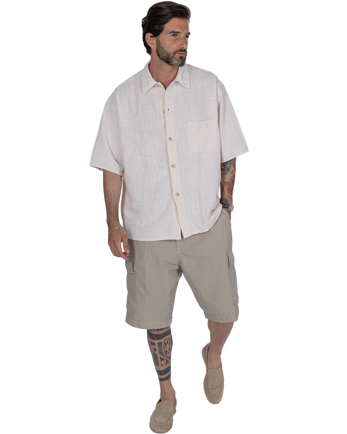 Men's cream linen short sleeve button-up shirt with chest pocket, paired with beige cargo shorts and tan loafers.