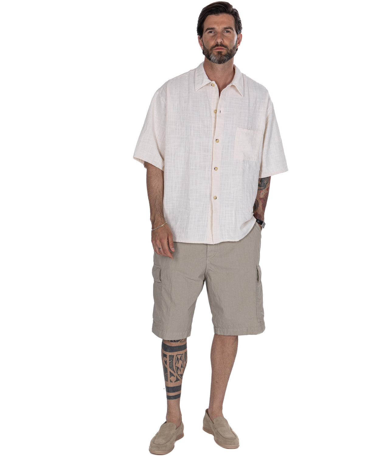 Men's cream linen short-sleeve button-up shirt with relaxed fit, paired with beige cargo shorts and suede loafers.