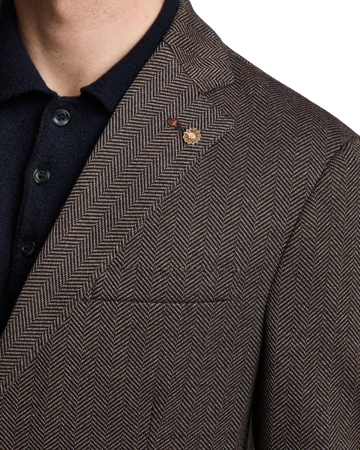 Brown herringbone blazer with a lapel pin, featuring a textured fabric and tailored fit. Perfect for smart-casual occasions.