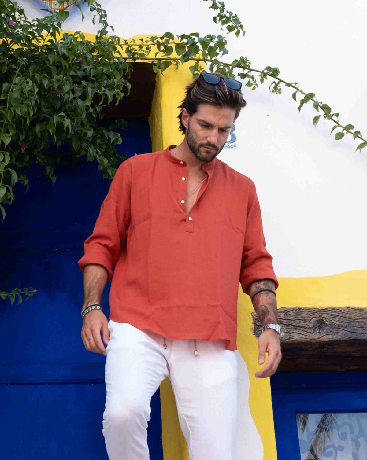 Men's rust orange linen henley shirt with white buttons, long sleeves, relaxed fit, paired with white pants.