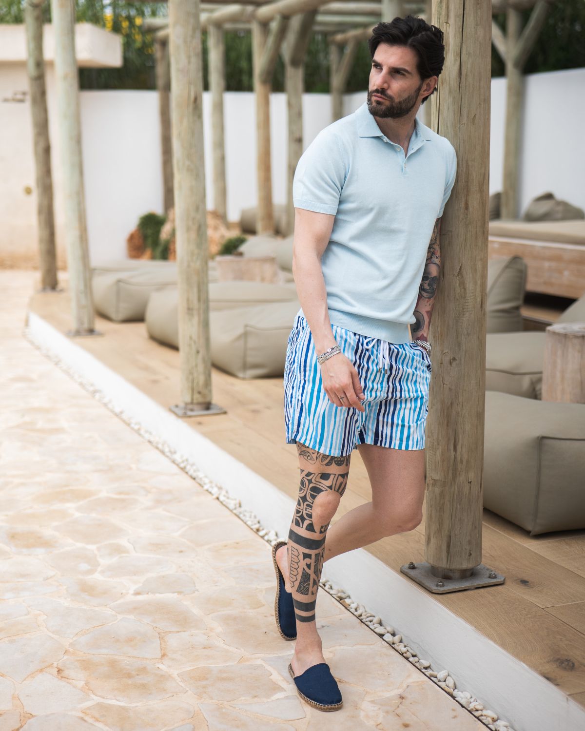 Light blue cotton polo shirt with blue and white striped swim shorts, casual summer resort wear for men.