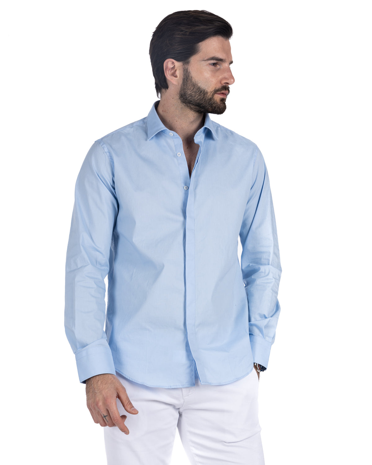 Men's light blue cotton shirt with hidden button placket and spread collar, worn with white trousers, side view