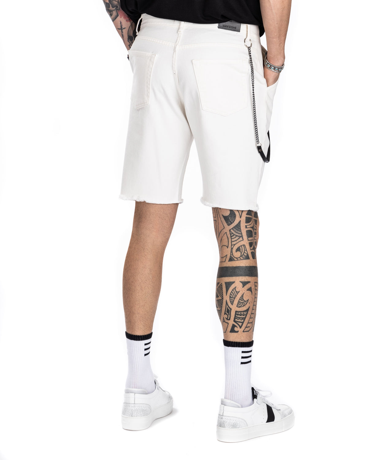 Close-up of men's off-white denim Bermuda shorts with button waist and black leather keychain, shown on a model