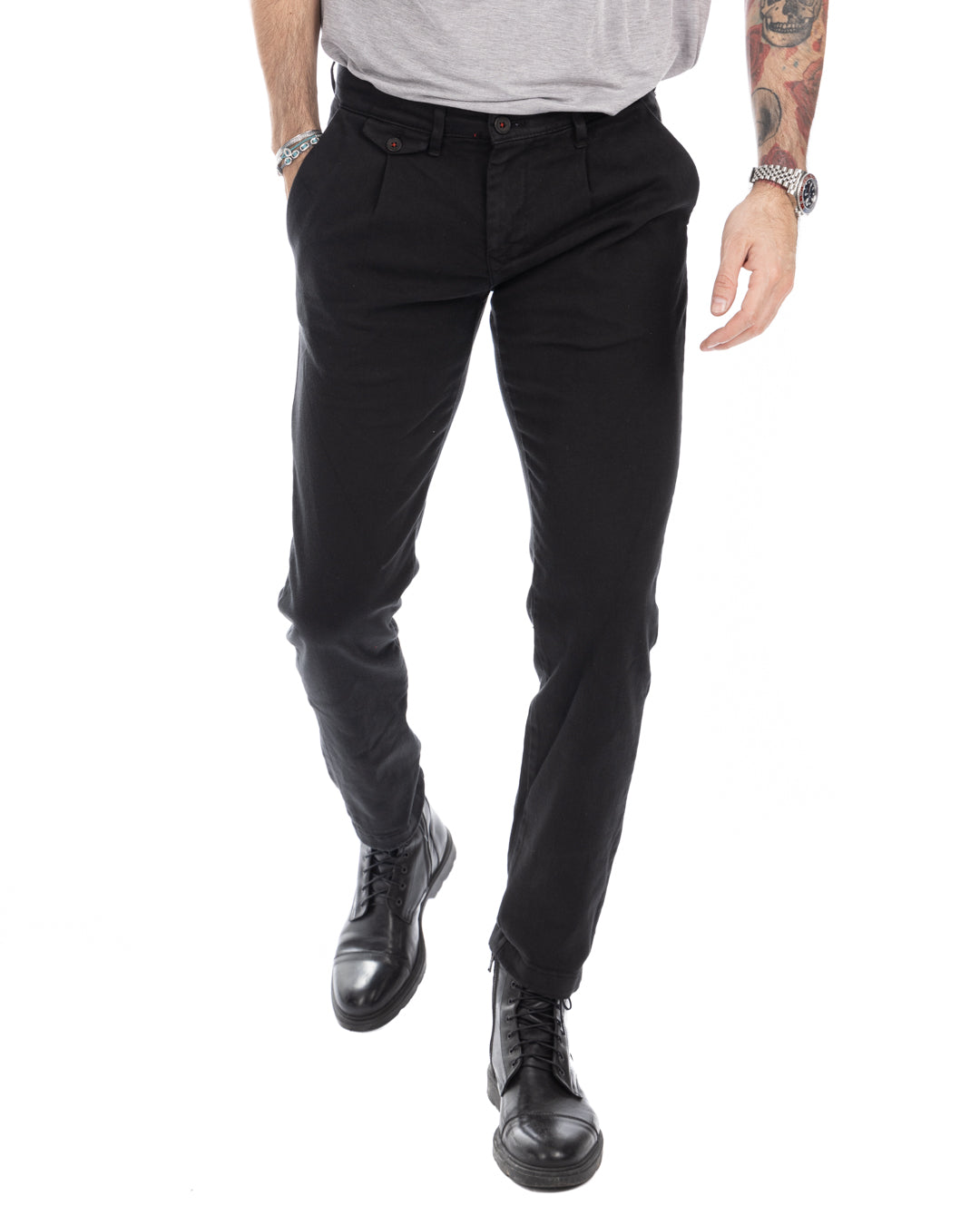 Men's black slim-fit cotton chinos with pleated front, paired with gray t-shirt and black leather boots.