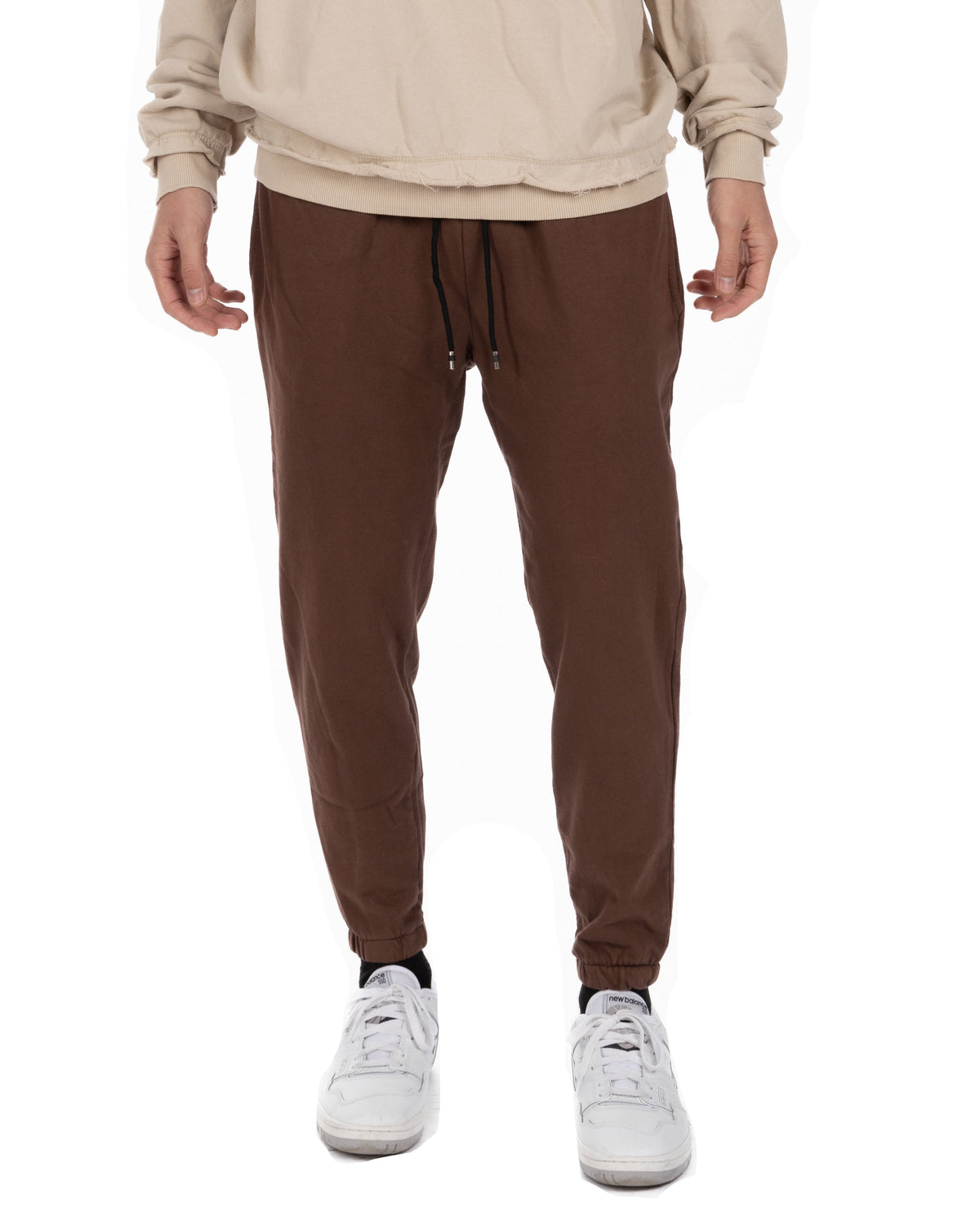 Men's brown cotton joggers with drawstring waist and cuffed ankles, paired with white sneakers.