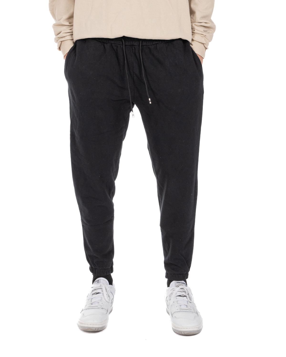Men's black cotton drawstring jogger pants worn with a beige long-sleeve top and white sneakers, front view